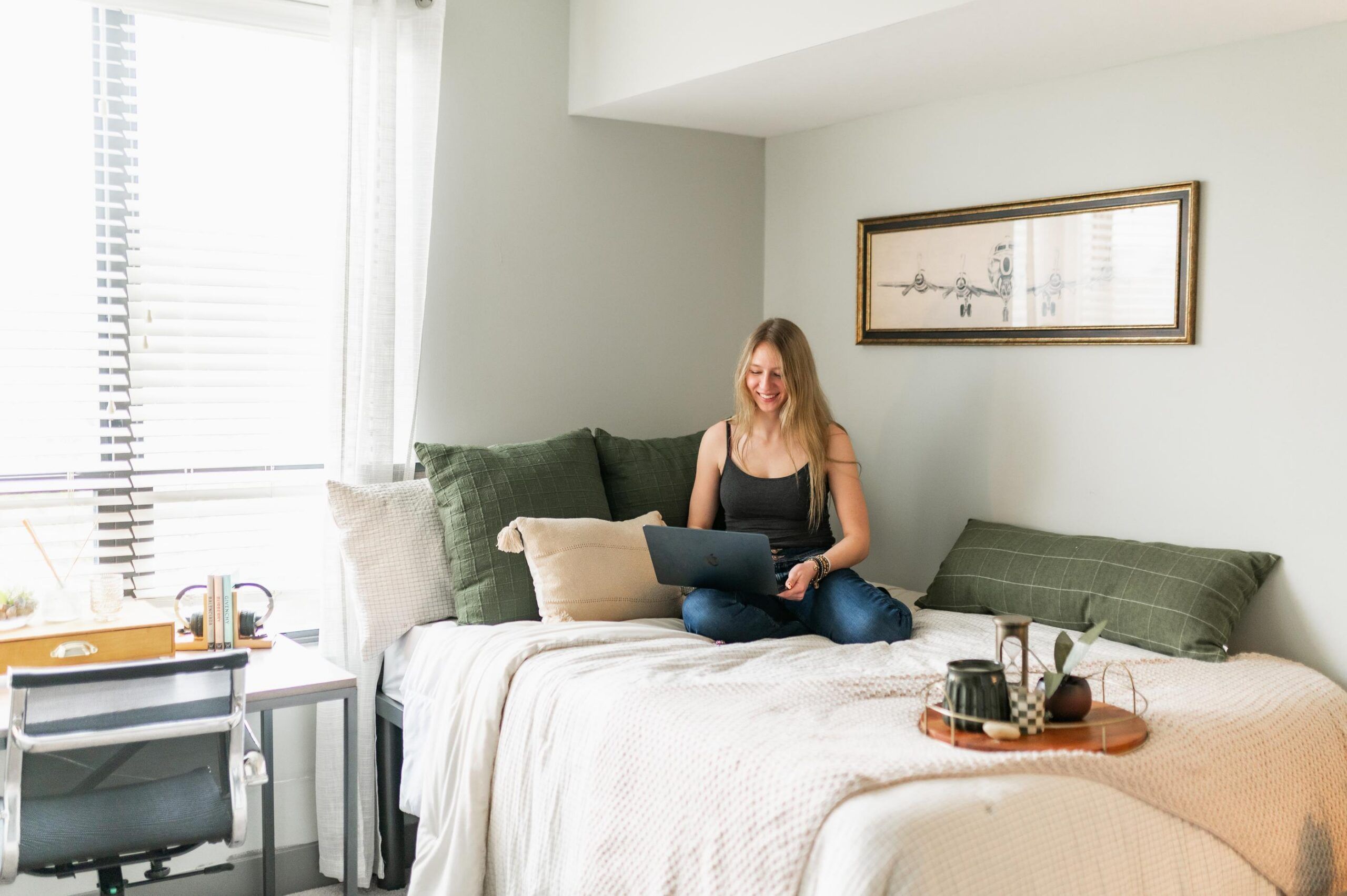 The Yard On South Main Student Living Apartments Woman sitting cross-legged on a bed using a laptop, with a tray of tea and snacks on the bed nearby.